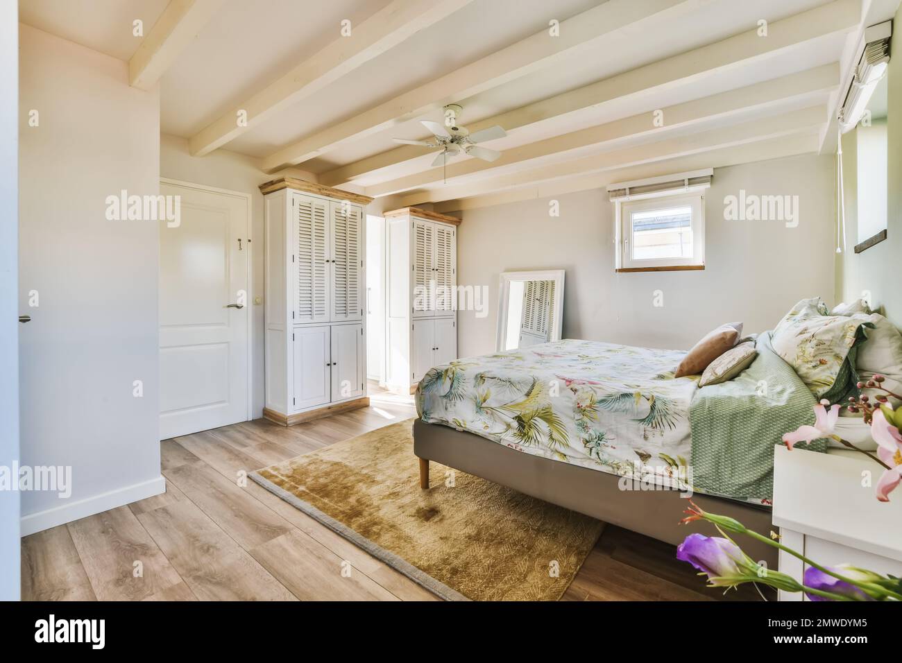 un dormitorio con paredes blancas y pisos de madera en el medio de la  habitación, hay una cama que tiene un edredón floral en ella Fotografía de  stock - Alamy