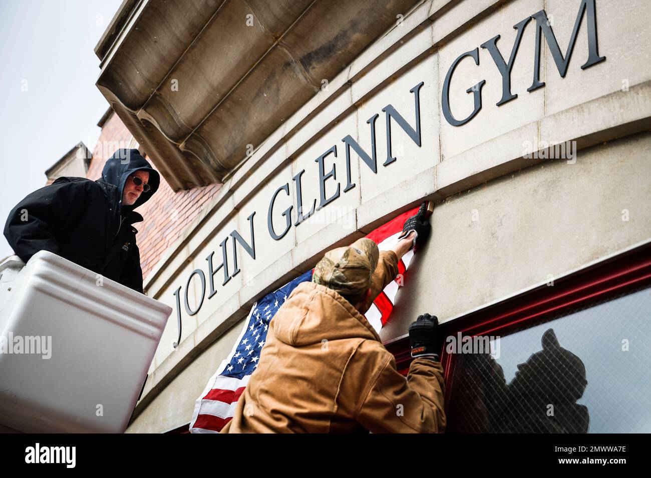 Workers install an American flag above the John Glenn Gym at the