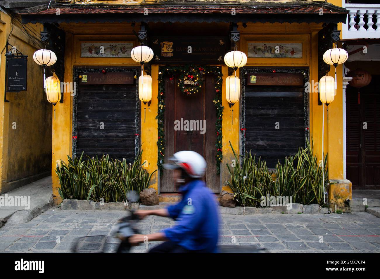 Hoi An Hombre en moto paseos en frente del edificio tradicional - Hoi, AN, Vietnam Foto de stock