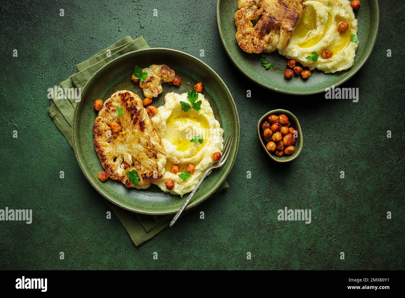 Vista superior de deliciosa coliflor asada con puré de papas y garbanzos harissa especiados servidos en un plato de cerámica sobre fondo de mesa verde Foto de stock