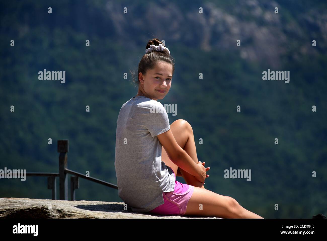 Joven adolescente, se sienta en la cima de Chimney Rock y disfruta del sol y la vista. Ella tiene en pantalones cortos rosados y camiseta gris. Foto de stock