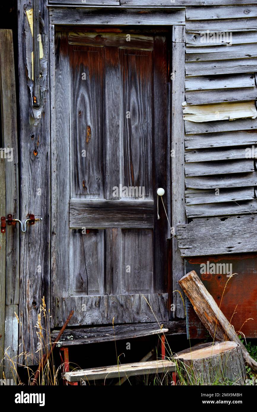 La puerta dilapidada tiene un pomo de puerta de porcelana blanca. La cuerda atada al marco de la puerta y la perilla mantienen la puerta cerrada. Puerta de marcos de madera desgastada y desgastada. Foto de stock