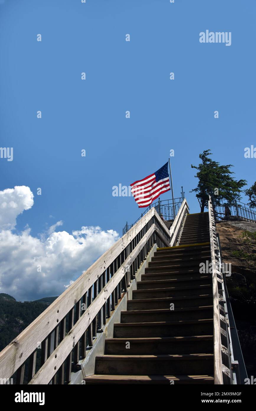 Escalones de madera conducen a la plataforma de observación en la parte superior de Chimney Rock en Chimney Rock State Park, Carolina del Norte. La bandera americana vuela en la plataforma. Foto de stock