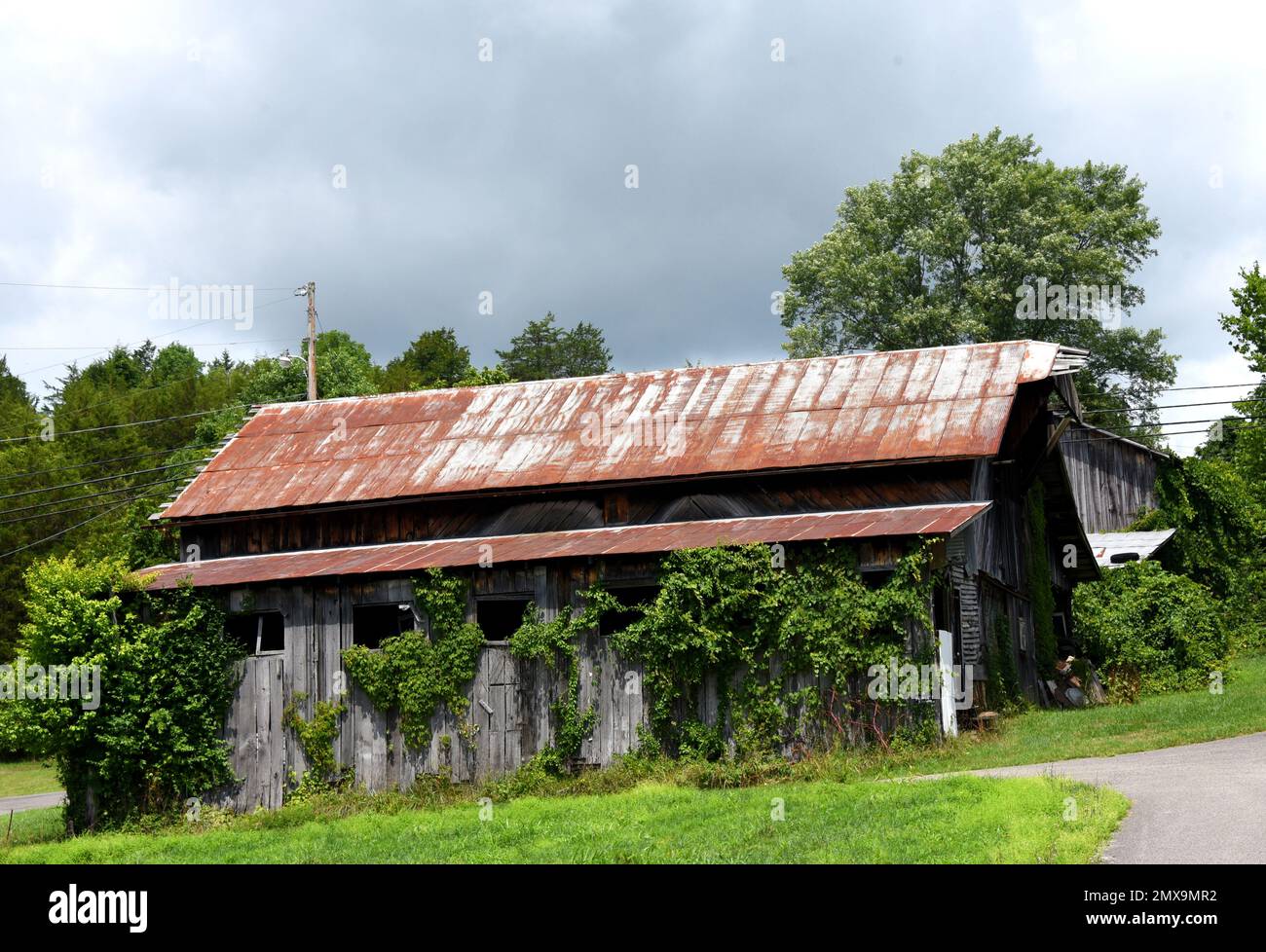 El granero de madera deteriorado, ubicado en Virginia, tiene un techo de hojalata oxidado y una hilera de ventanas cubiertas hacia abajo. Foto de stock