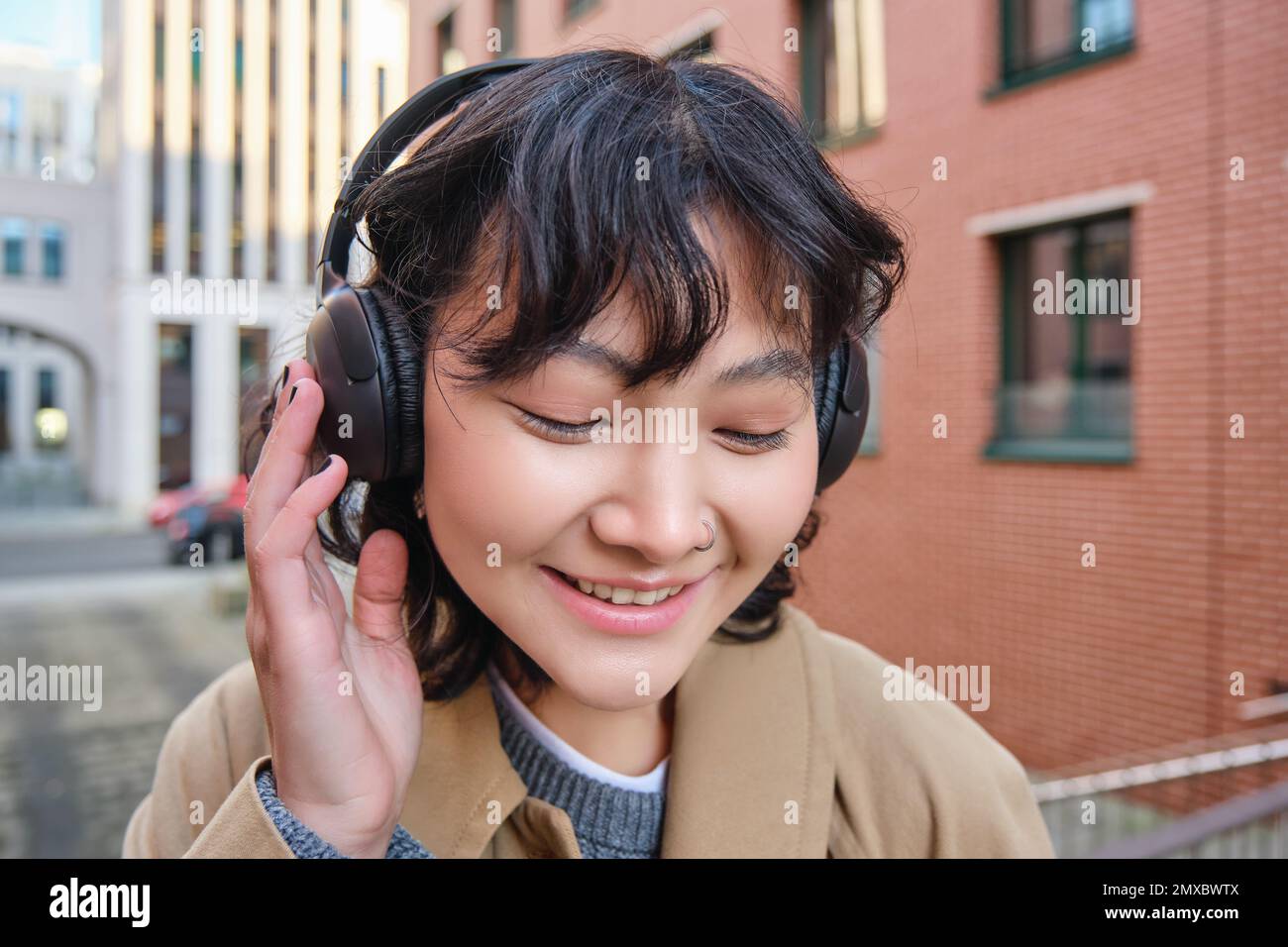 Close up retrato de la chica asiática morena elegante, escucha música en  auriculares, toca auriculares y sonríe, disfruta de la canción favorita, se  encuentra en la calle Fotografía de stock - Alamy