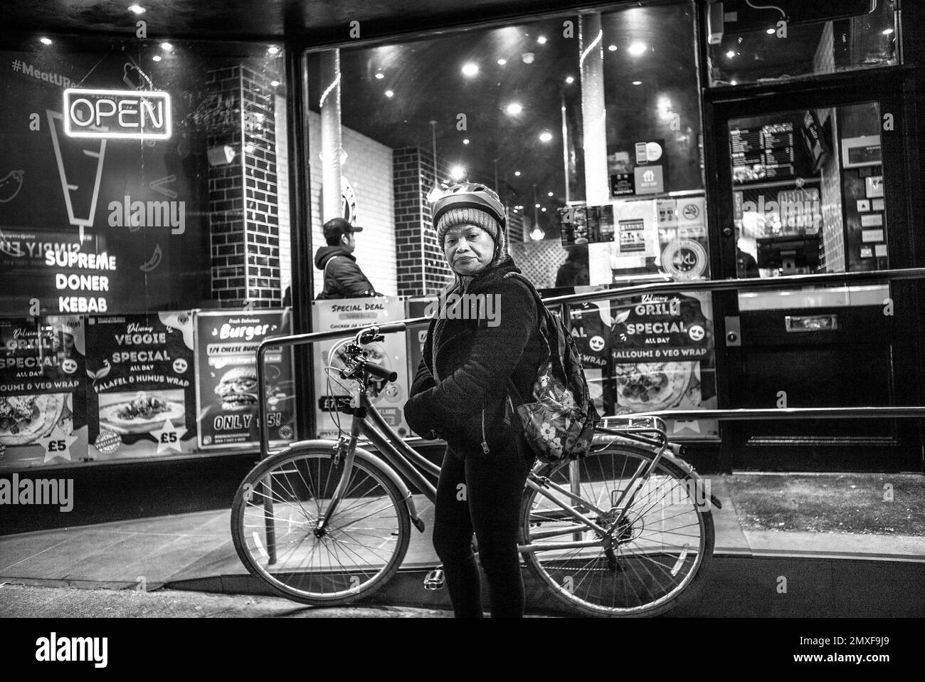 mujer que lleva sombrero de lana y casco de ciclismo mira directamente a la lente de la cámara esperando al lado de la bicicleta Foto de stock