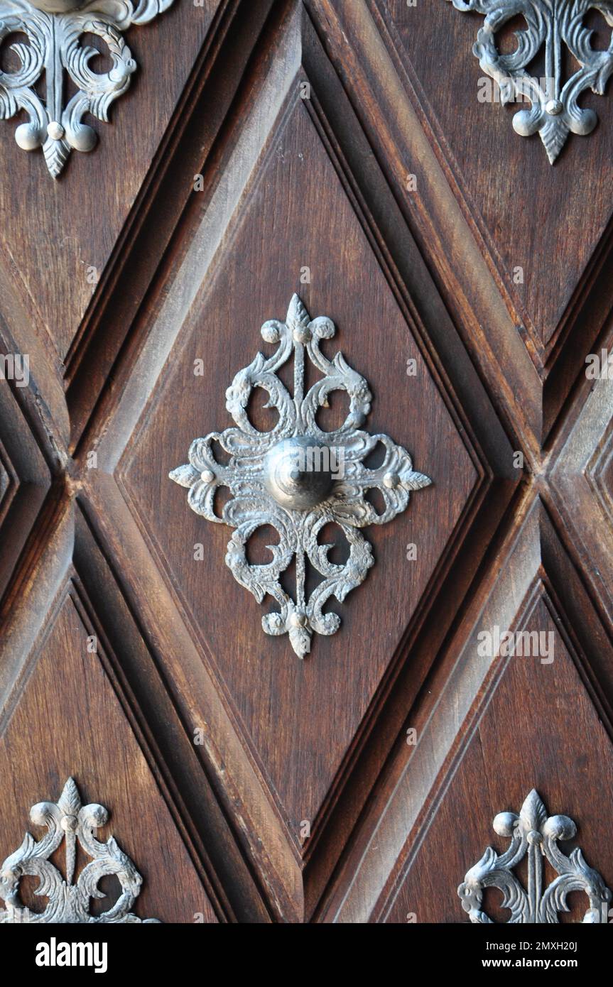 Puerta de madera antigua con decoración de metal en cubos de madera. Detalle de una puerta en madera marrón con motivos plateados realizados con mucho arte .Highlight para el pomo Foto de stock