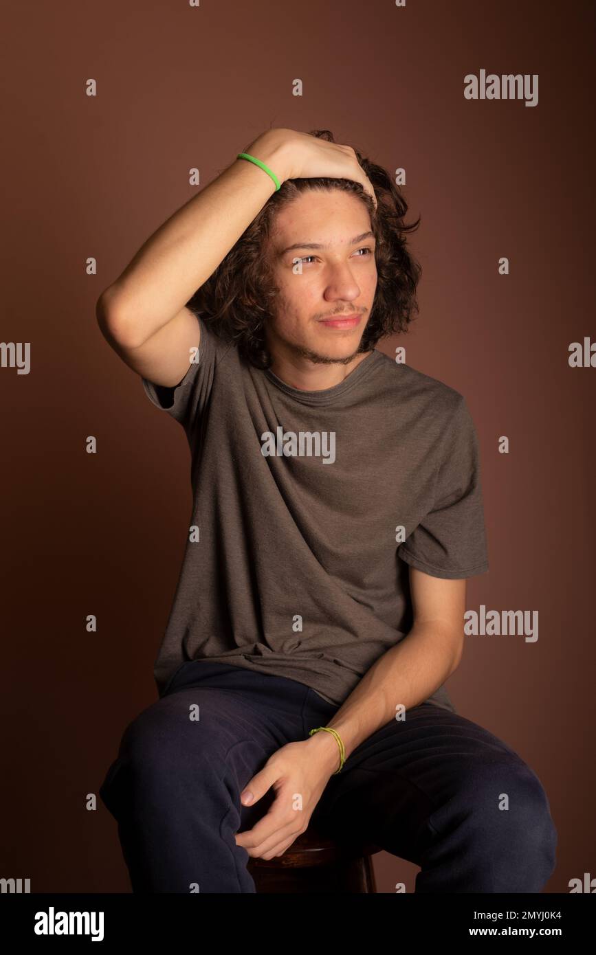 Joven guapo, sentado, con la mano en la cara. Aislado Bisque fondo. Foto de stock