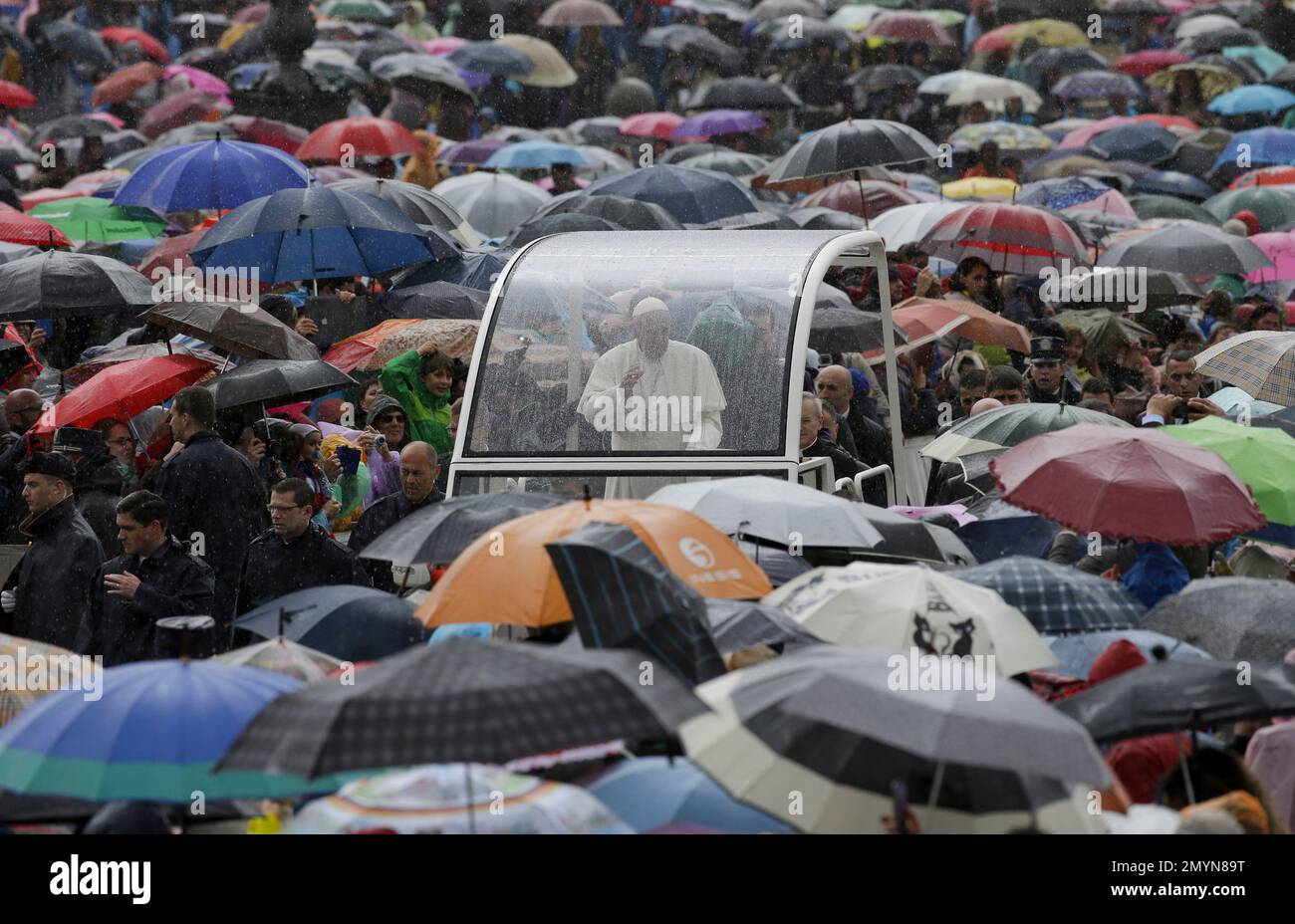 Pope Francis is driven through the crowd sheltering itself from the rain under umbrellas as he