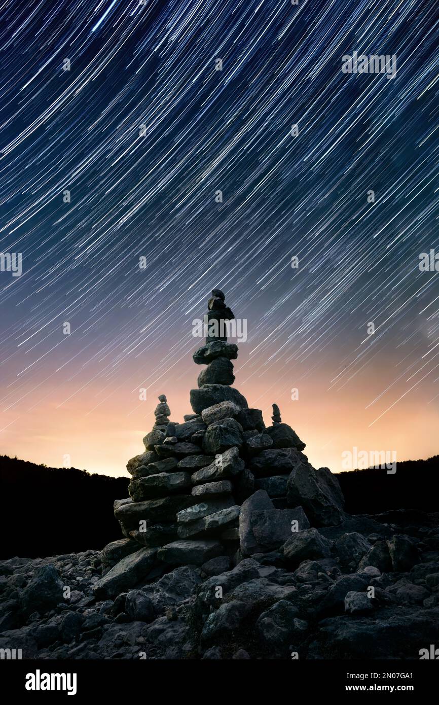 Cielo nocturno con rastros de estrellas sobre arreglo de piedra equilibrada apilada, composición vertical centrada Foto de stock