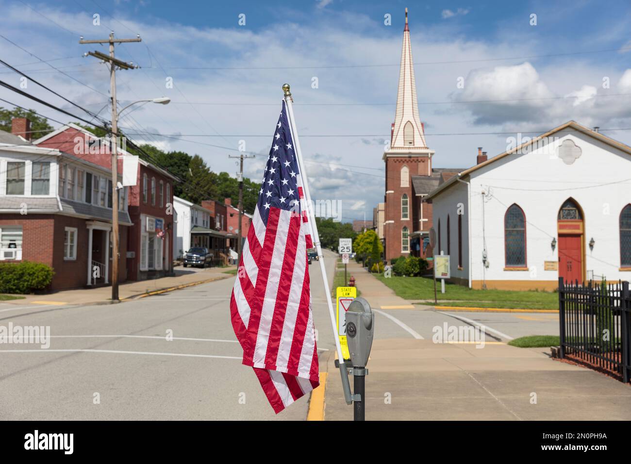 Bandera americana volando en una calle principal tranquila con casas y una iglesia. Foto de stock