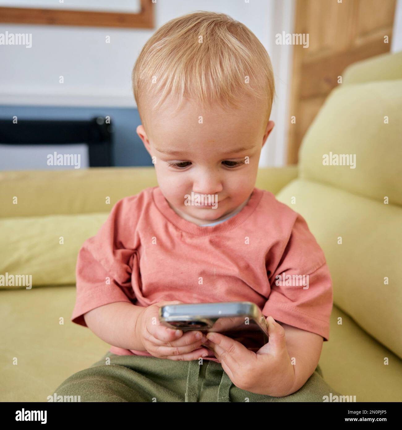 Niño pequeño sosteniendo teléfono inteligente con expresión animada en el interior Foto de stock