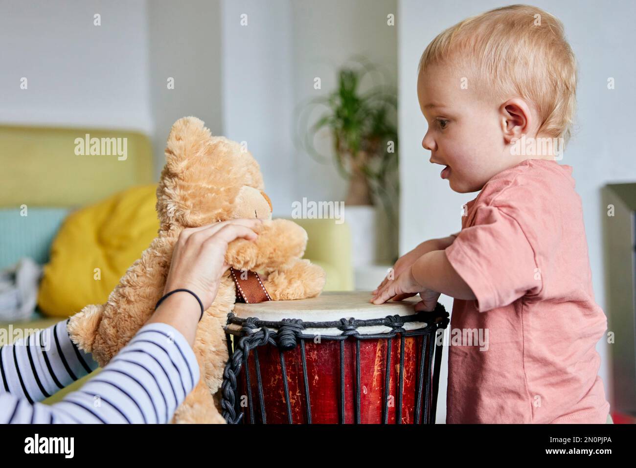 Niño pequeño y osito de peluche tocando bongo tambor juntos en casa Foto de stock