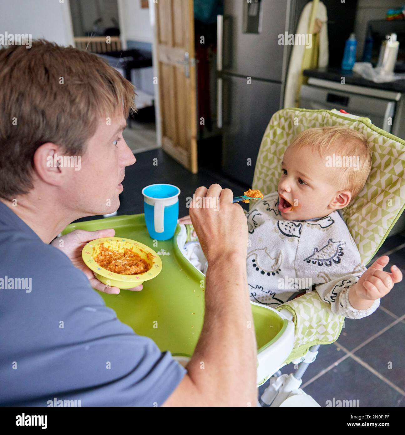 Padre alimentando al niño pequeño en silla alta en la cocina Foto de stock