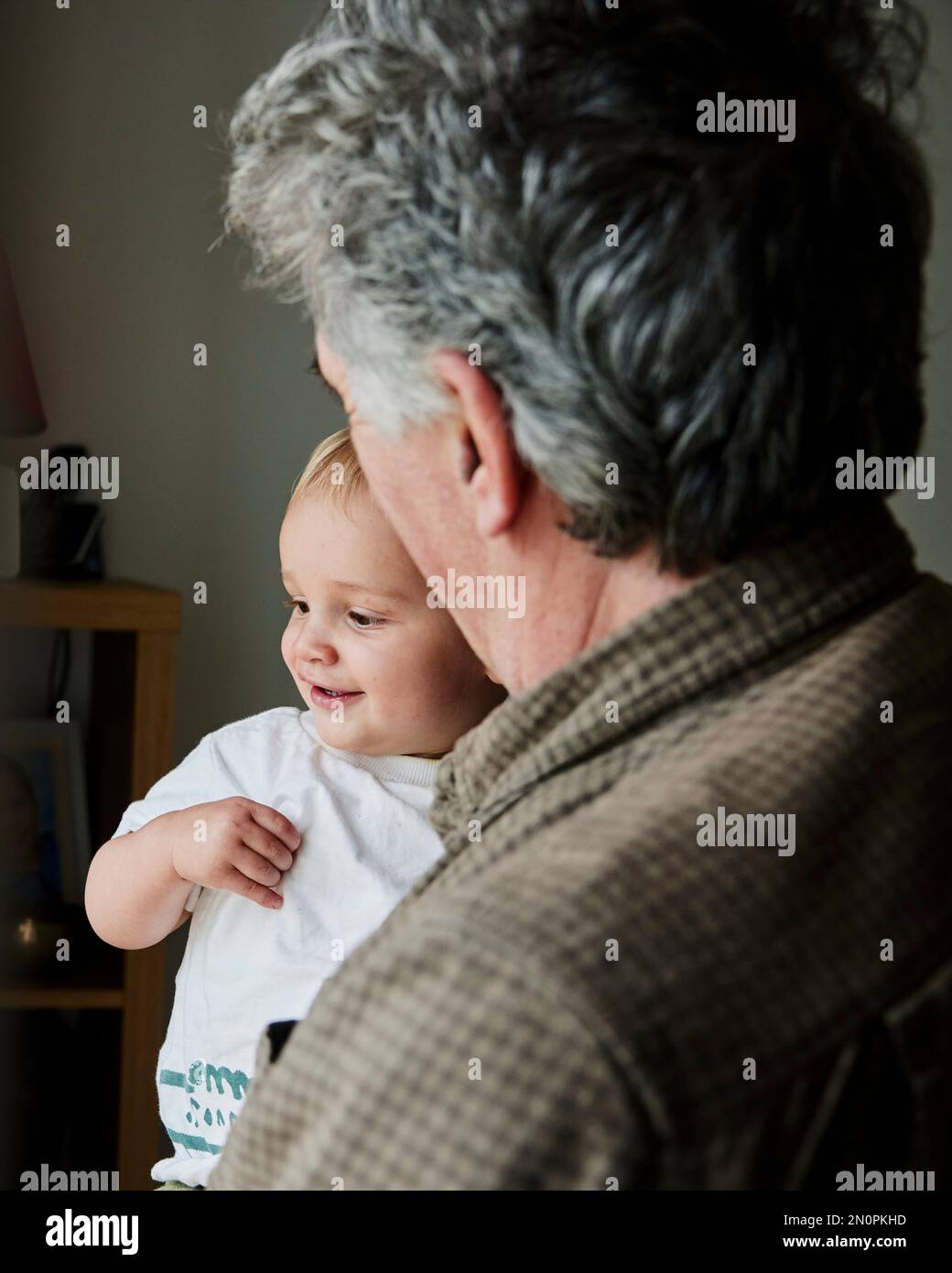 Cerca del niño sonriente en brazos del abuelo mirando por la ventana Foto de stock