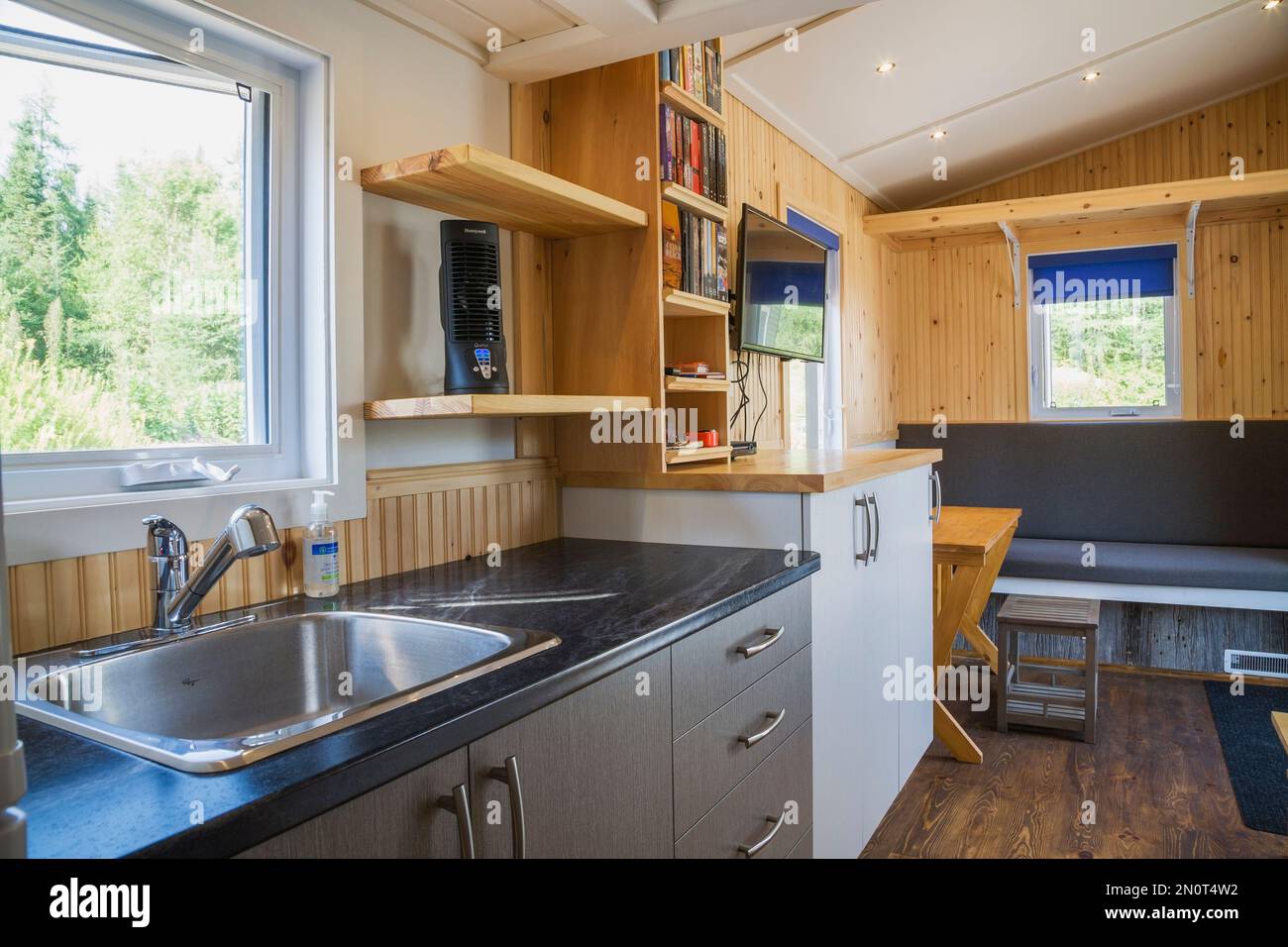 Encimera de cocina de arborita negra con gabinetes de melamina gris y  blanco, vista de la sala de estar principal con mesa de comedor de madera  de pino expandible dentro del contenido
