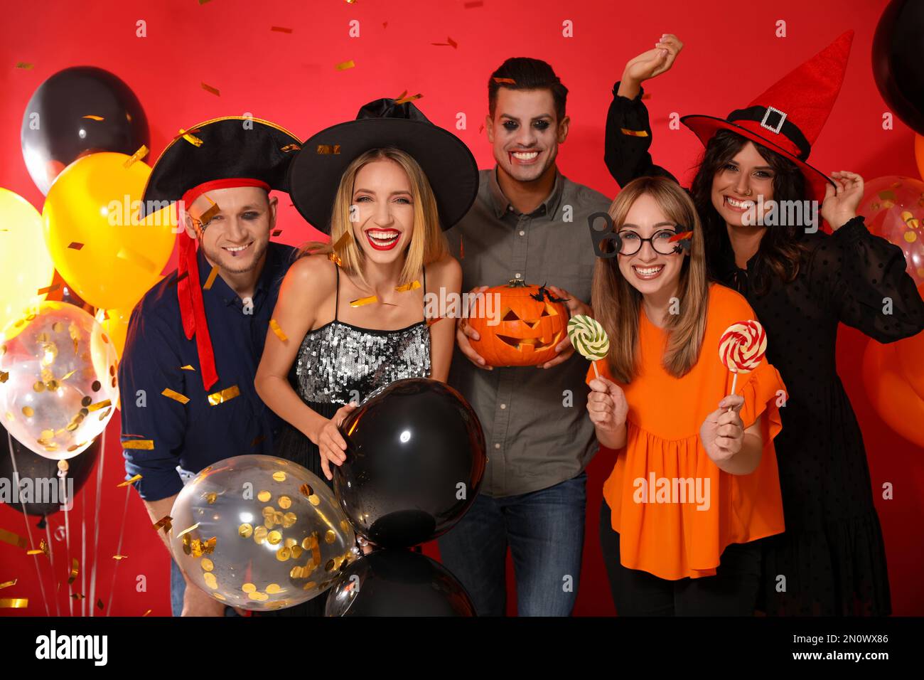 Amigos felices en disfraces con accesorios de fiesta de Halloween sobre  fondo rojo Fotografía de stock - Alamy