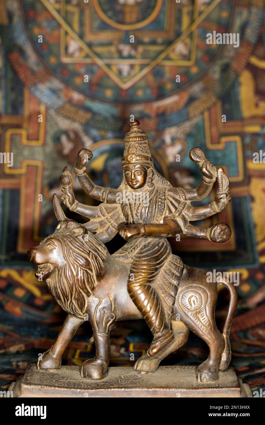Figura de bronce de la diosa india Durga montando en una figura de león, fotografía de estudio con una thangka tibetana en el fondo Foto de stock