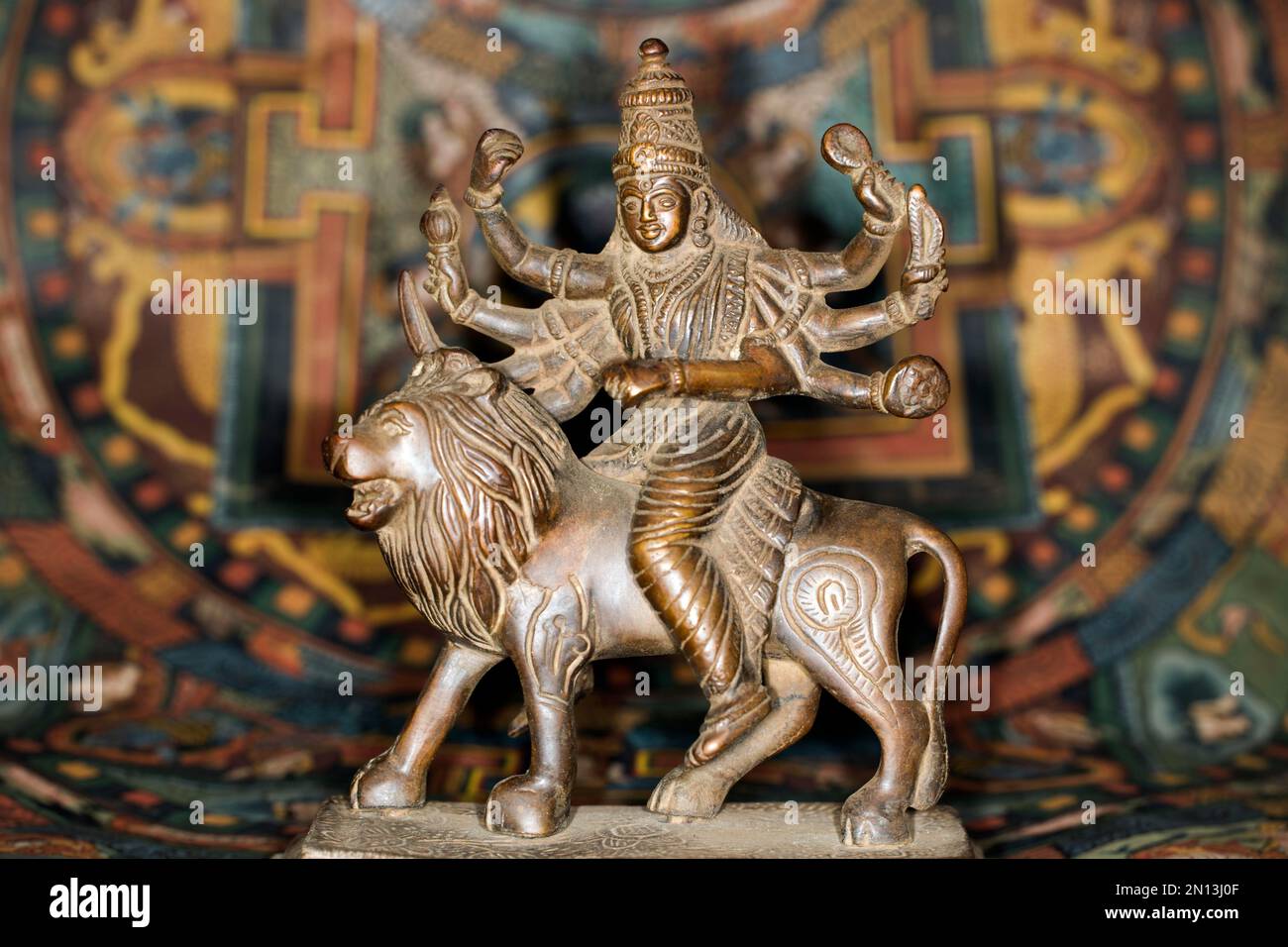 Figura de bronce de la diosa india Durga montando en una figura de león, fotografía de estudio con una thangka tibetana en el fondo Foto de stock