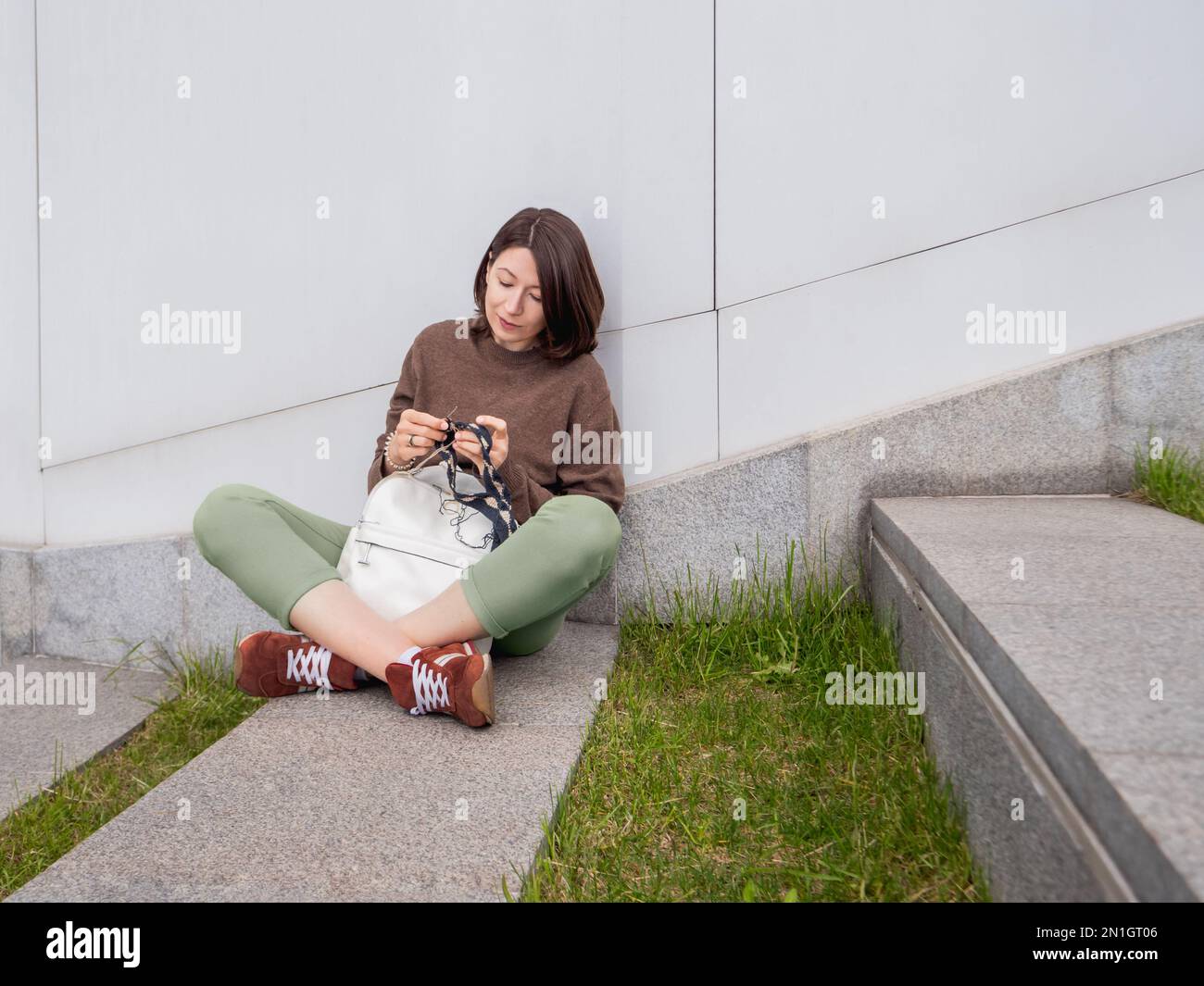 La mujer está tejiendo al aire libre. Ocio tranquilo de la hembra en parque urbano. Pasatiempo anti-estrés. Foto de stock