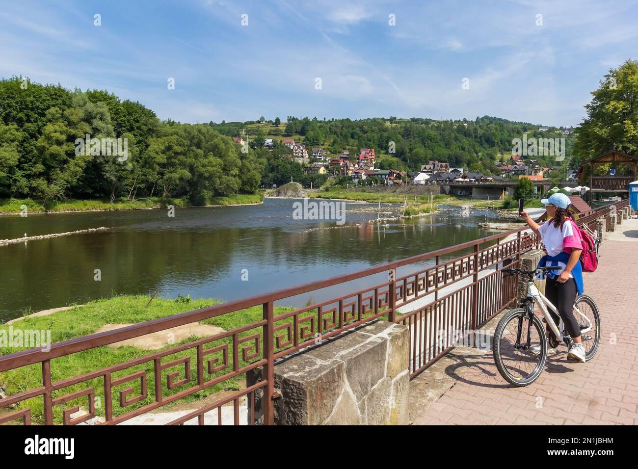 Mujer joven en una bicicleta tomando fotos con el teléfono móvil del río Dunajec en Szczawnica, Polonia Foto de stock
