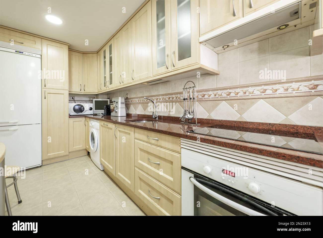 Cocina en forma de L con armarios de madera clara con electrodomésticos  blancos y encimeras de granito rojo pulido Fotografía de stock - Alamy