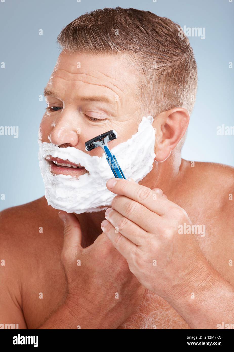 Cara, crema de afeitar y hombre con la maquinilla de afeitar en estudio  aislado en un fondo gris para la depilación. Limpieza, cuidado de la piel y  modelo masculino senior con facial