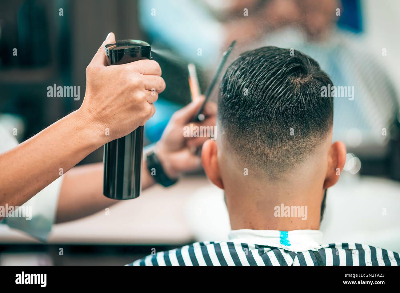 Vista posterior del cliente masculino que tiene corte de pelo mientras que el peluquero de cosecha moja el pelo en la barbería moderna Foto de stock