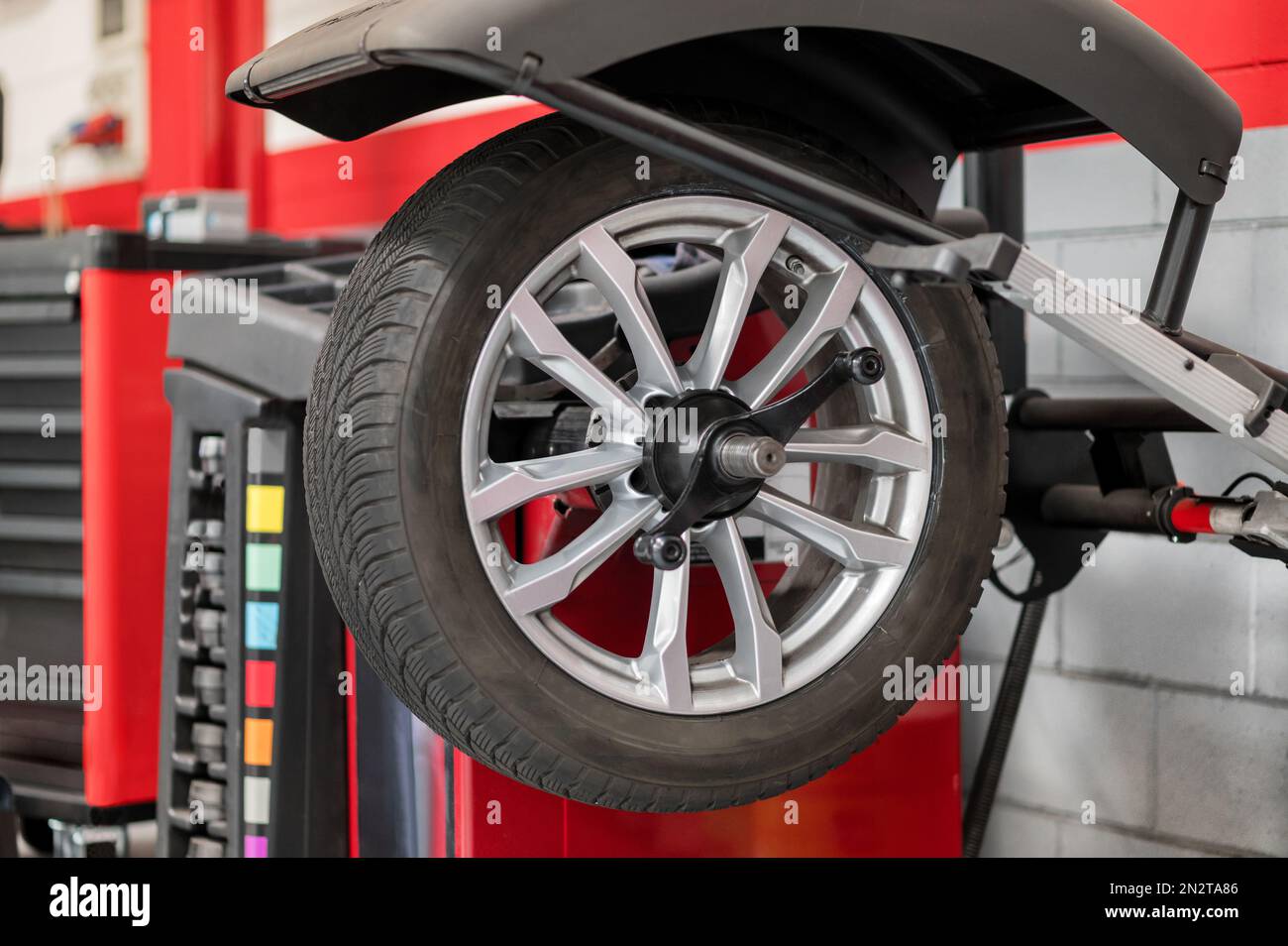 Rueda que cuelga en el equilibrador de la rueda durante el servicio del coche dentro de la tienda moderna del distribuidor del coche Foto de stock