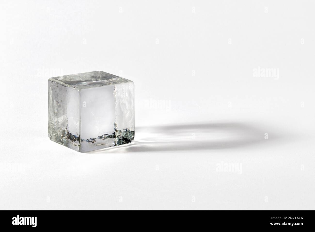 Cubo de cristal limpio hecho de vidrio frágil transparente que proyecta sombra sobre fondo gris Foto de stock