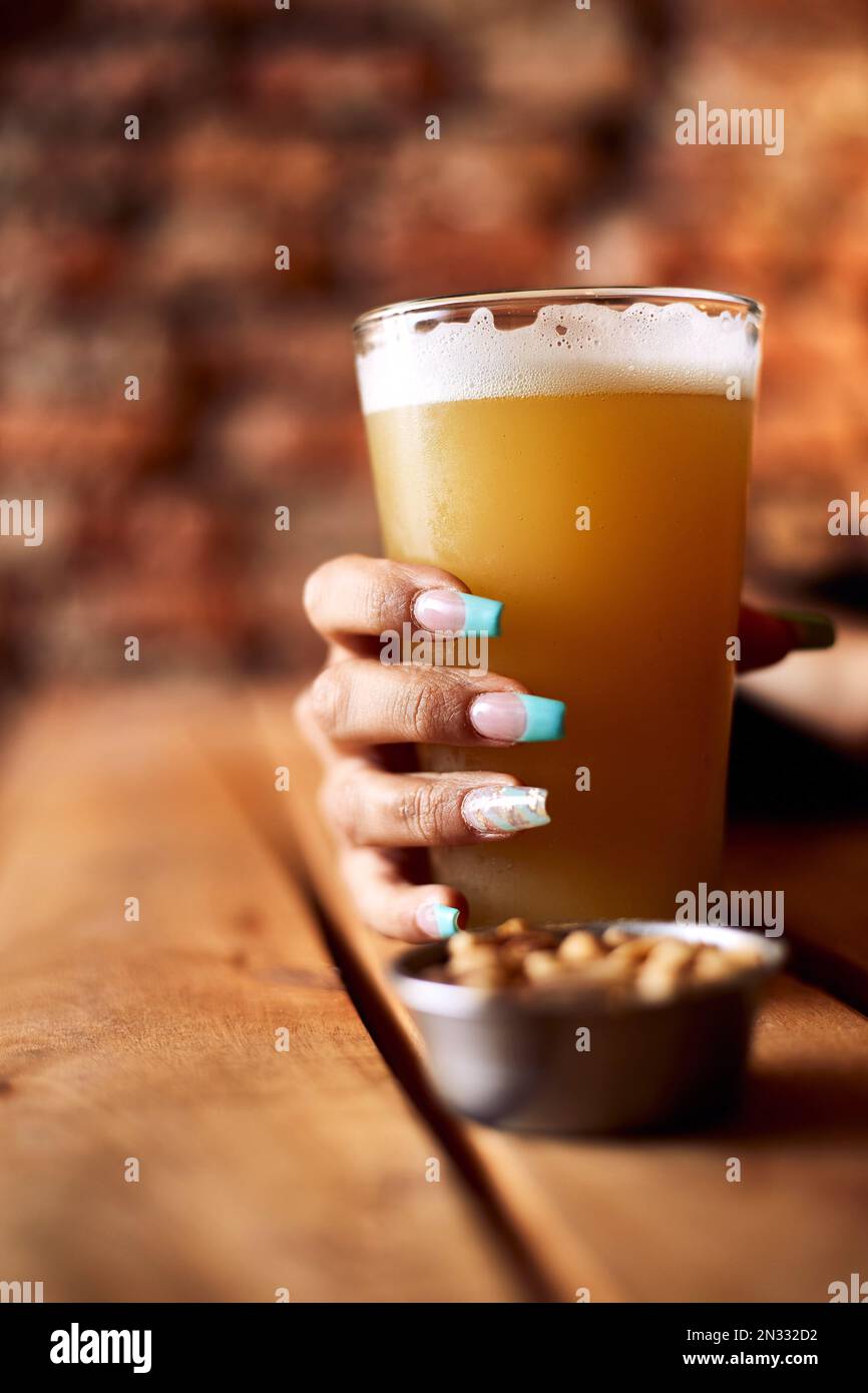 Un tiro vertical de una mujer con uñas pintadas sosteniendo una pinta de cerveza en un pub Foto de stock