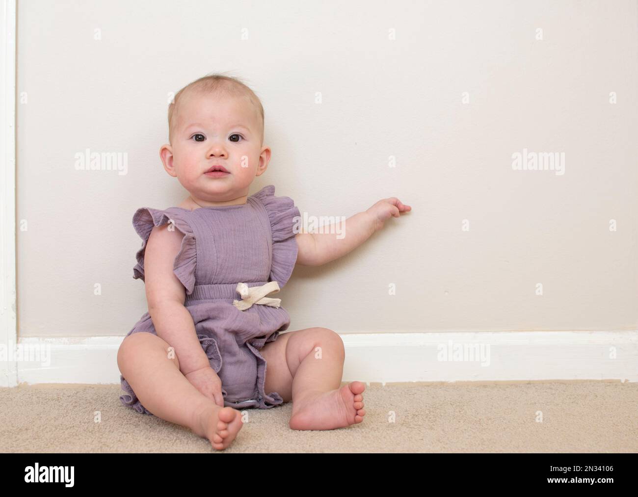 Lindo bebé caucásico aprendiendo a sentarse a los 9 meses de edad Foto de stock