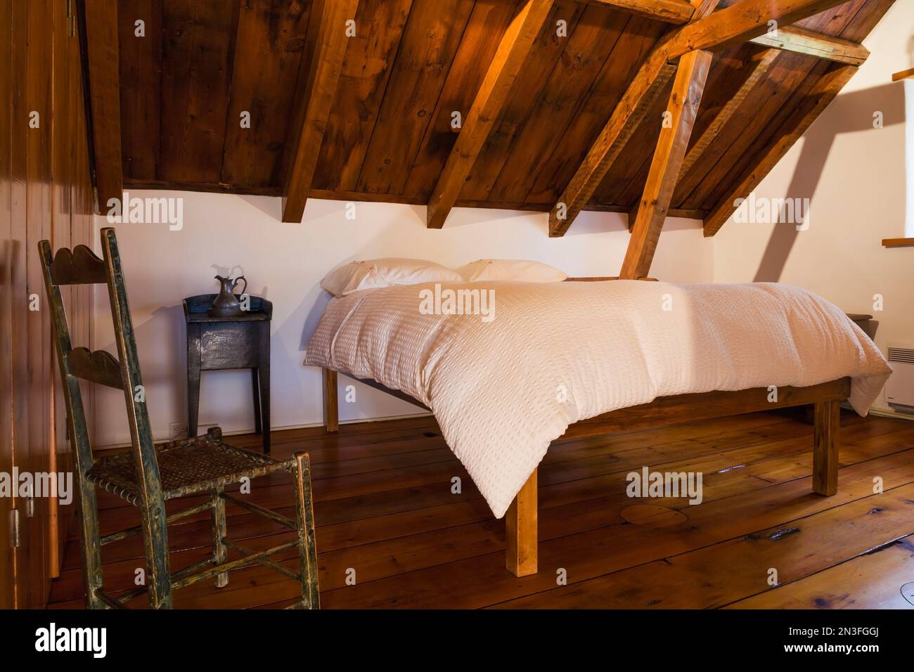 Cama de marco de madera tamaño queen hecha a mano y silla de madera antigua  con asiento de cuero de vaca tejido en el dormitorio principal en el piso  de arriba dentro