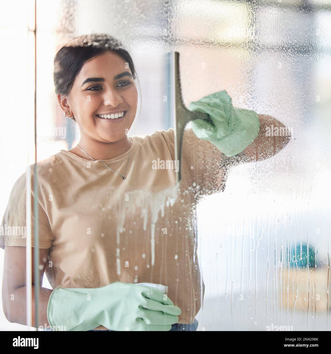 Feliz, sonrisa y niña que limpia la ventana con la botella de spray y