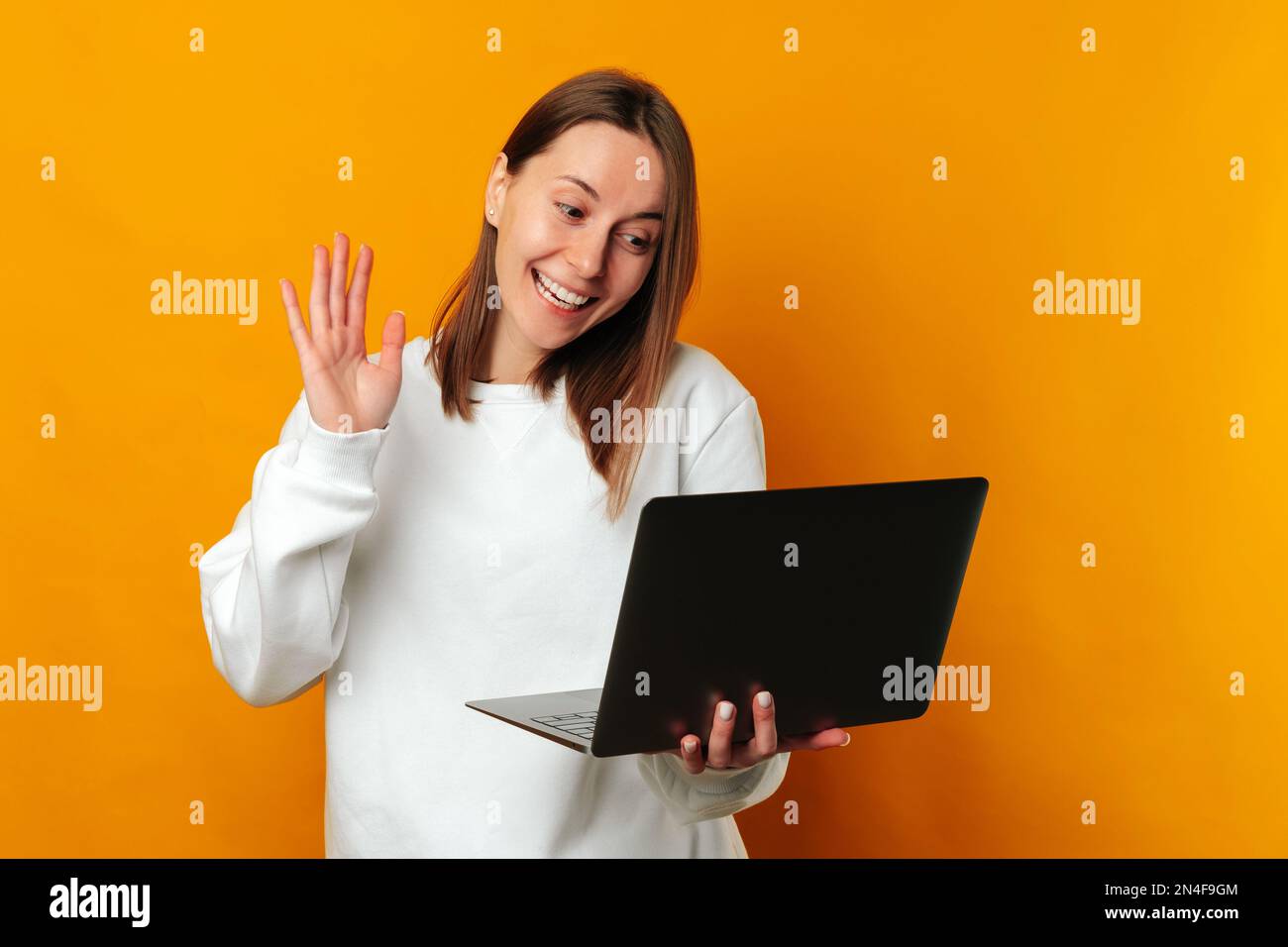 La mujer sonriente joven está teniendo una videollamada en su computadora  portátil y diciendo hola sobre fondo amarillo Fotografía de stock - Alamy