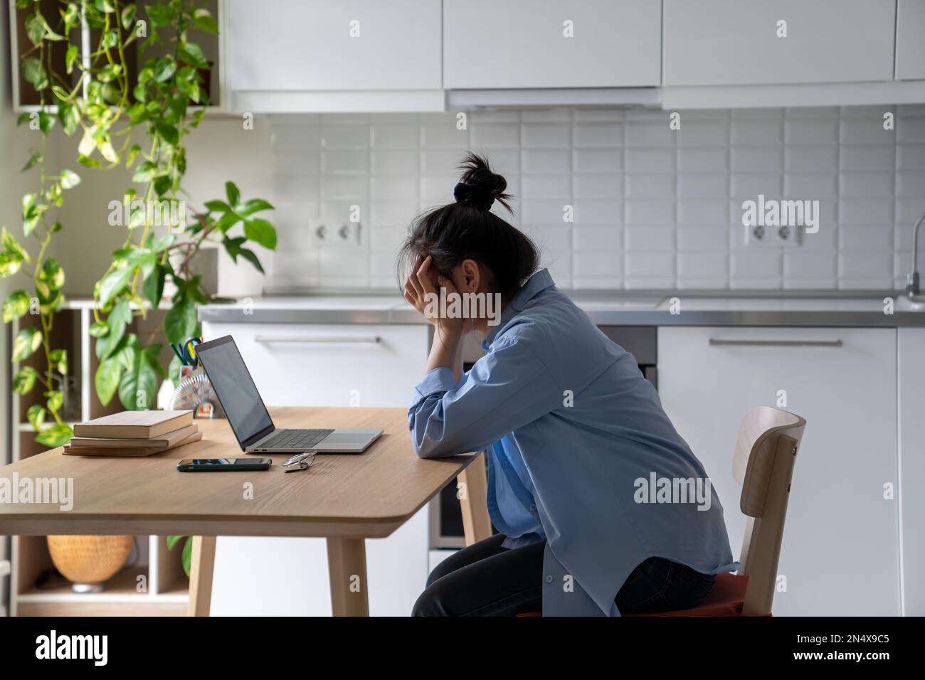 Mujer joven infeliz sentada en la mesa de la cocina mirando el ordenador portátil que tiene problemas en la búsqueda de trabajo Foto de stock