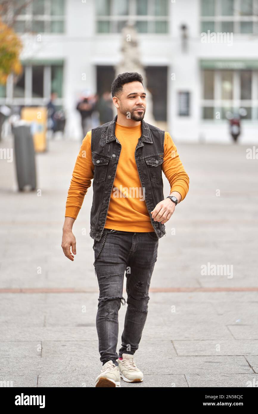 Hombre latino caminando por las calles de la ciudad con suéter naranja y  chaleco negro Fotografía de stock - Alamy