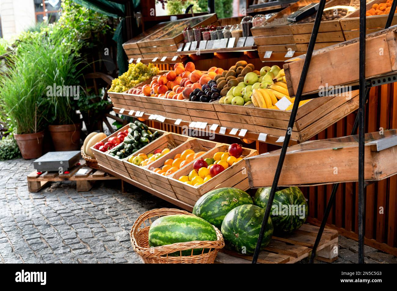 Puesto de fruta en un mercado callejero exterior con sandías orgánicas, naranjas, limones en cajas de madera pequeña empresa vegana comida saludable Foto de stock