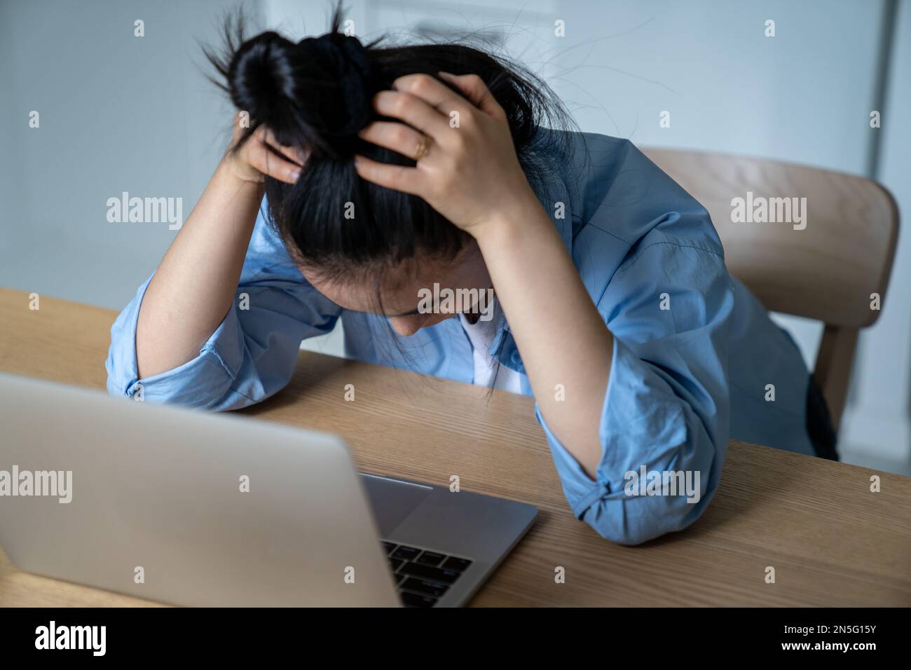 Mujer estresada que se sienta en el escritorio con el ordenador portátil que sostiene la cabeza en las manos que tiene problemas de negocio en línea Foto de stock