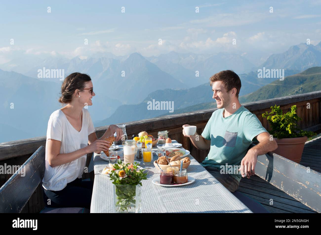 Joven pareja desayunando en la terraza y sonriendo, Zillertal, Tirol, Austria Foto de stock