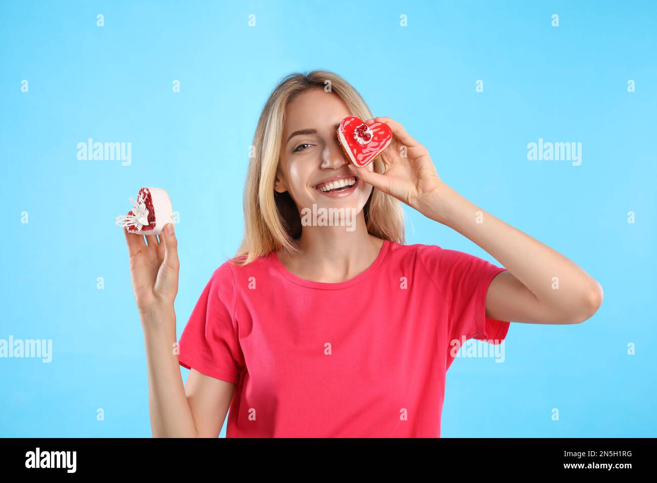 Concepto de elección entre comida sana y chatarra. Mujer con pasteles sobre fondo azul claro Foto de stock