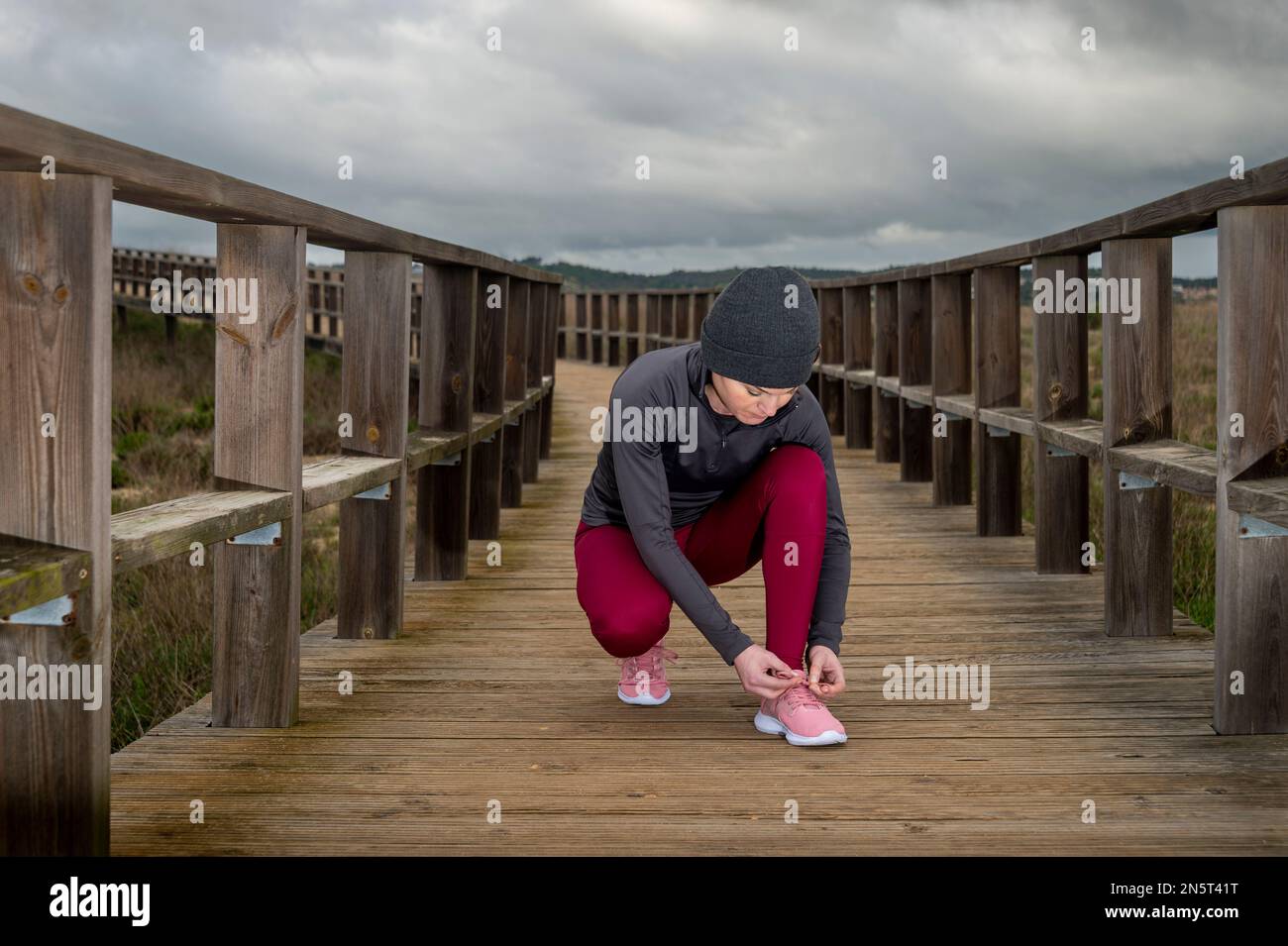Mujer jogger atando su cordón de zapatos, preparación para una carrera en un paseo marítimo de madera Foto de stock