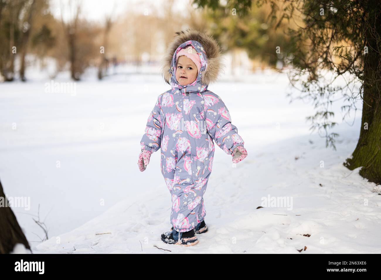 La niña usa traje de nieve infantil un soleado de invierno Fotografía de stock -