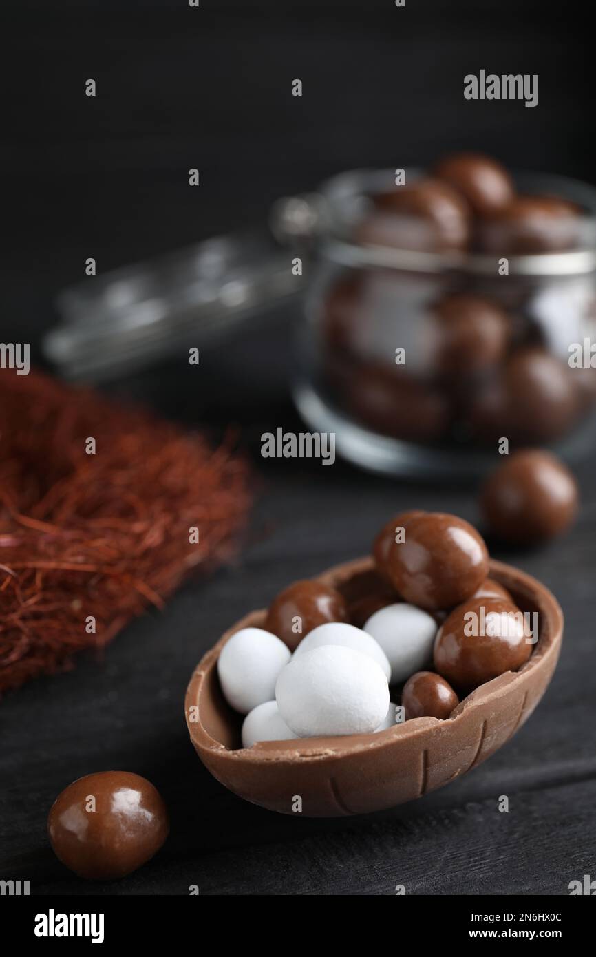 La mitad de sabroso huevo de chocolate con dulces en la mesa de madera negra, espacio para el texto Foto de stock