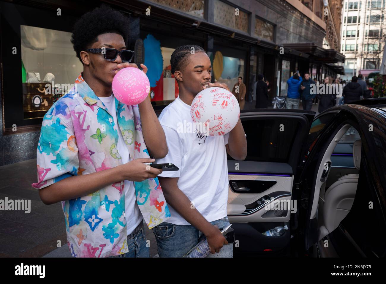 Hombres jóvenes inflan globos de cumpleaños fuera de Harrods, el 9th de febrero de 2023, en Londres, Inglaterra. Foto de stock