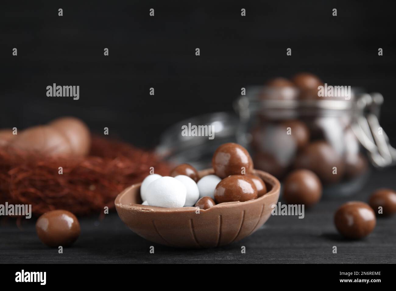 La mitad de sabroso huevo de chocolate con dulces en la mesa de madera negra, espacio para el texto Foto de stock