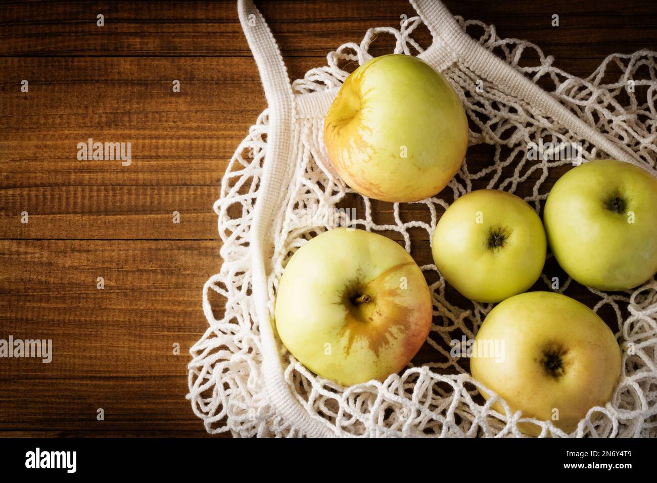 Bolso neto de algodón con manzanas de frutas sobre fondo de madera oscura. Estilo de vida sostenible. Bolsa de compras reutilizable, forma de vida sostenible. Ambiente ecológico Foto de stock
