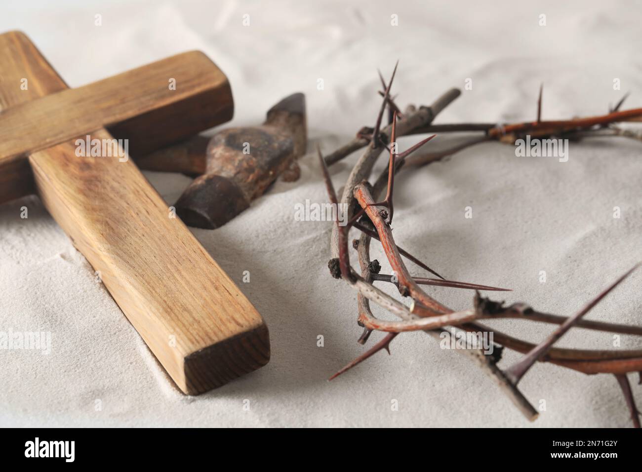 Corona de espinas, cruz de madera y martillo sobre arena. Atributos de Pascua Foto de stock