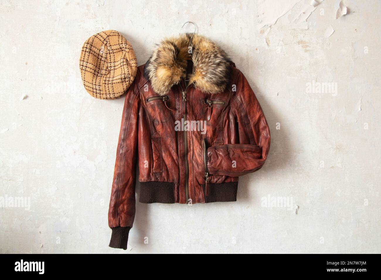 chaqueta de cuero rojo y tapa de cuadros colgando en la pared vieja blanca, moda Foto de stock