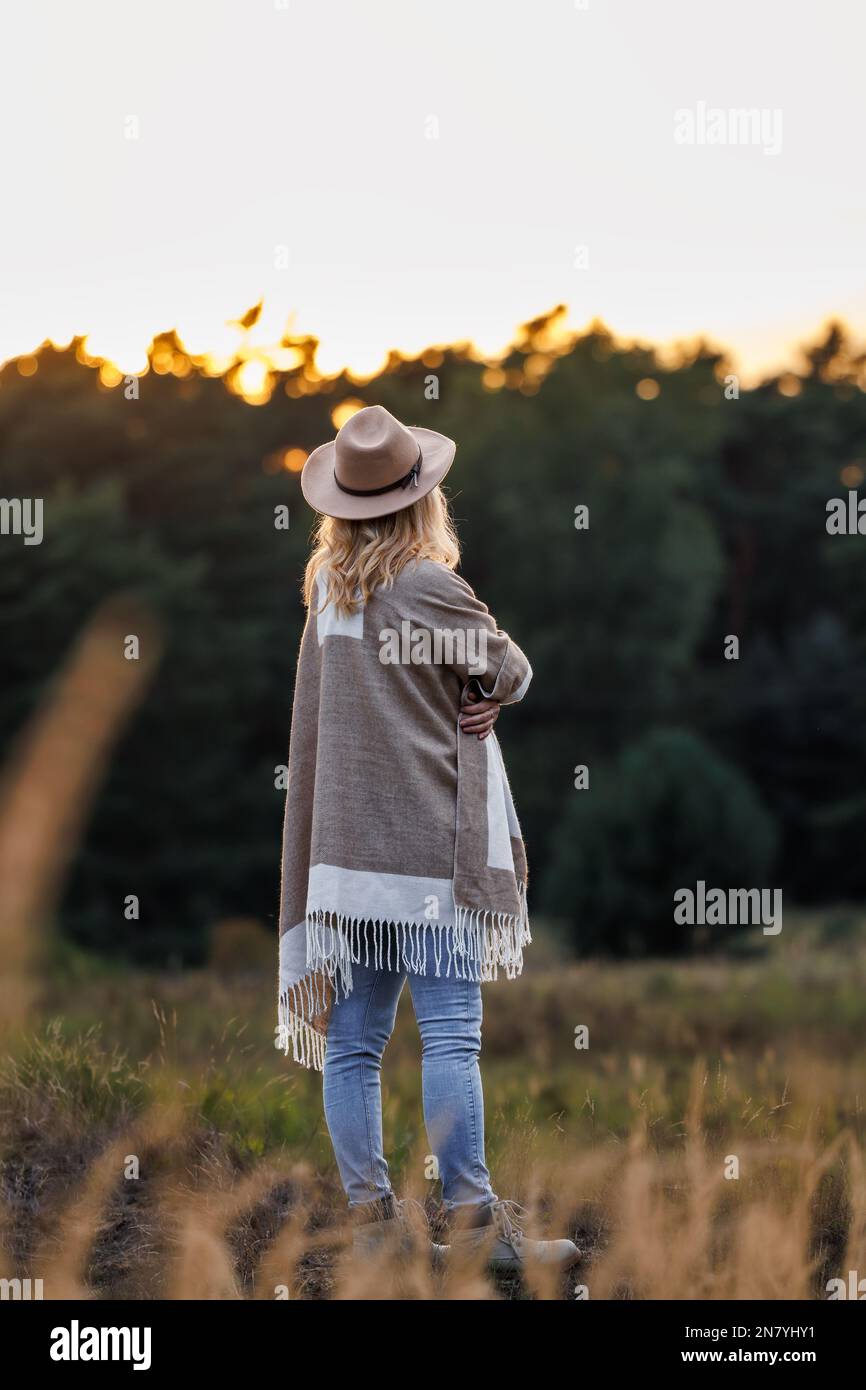 Mujer con poncho y sombrero de vaquero disfrutando de la puesta de sol en  la naturaleza. Persona femenina que lleva estilo de moda boho Fotografía de  stock - Alamy